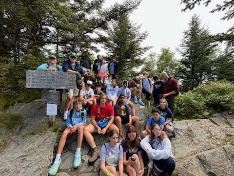School group sitting on rocks at a trail sign